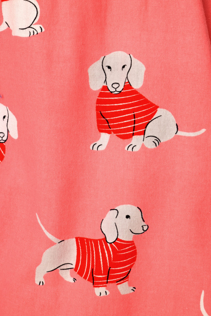 A close-up of a pink fabric with a repeating pattern of dachshund dogs wearing red striped sweaters.