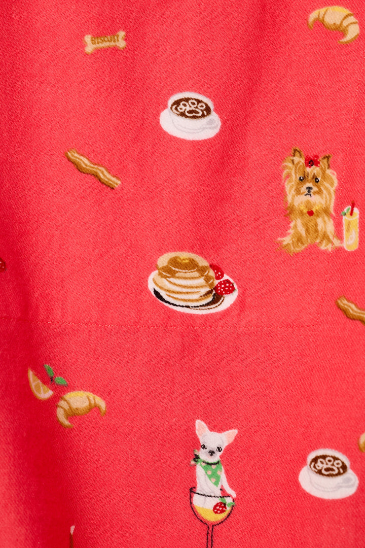 A close-up of a dark coral fabric with a whimsical, printed pattern featuring pancakes, croissants, coffee cups, bacon strips, and small dogs ready for brunch.