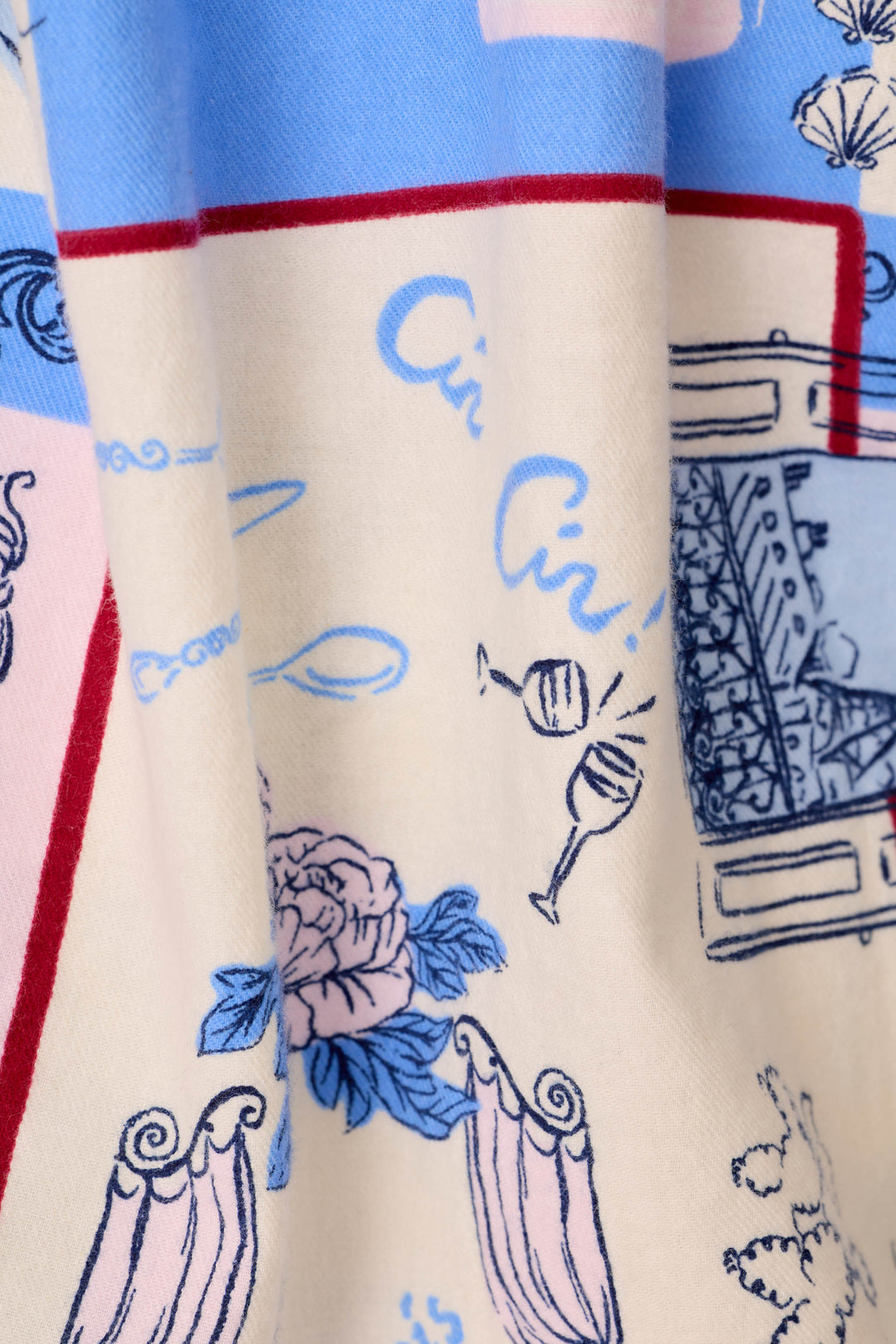 A close-up of a printed fabric with a cream background, light blue script text, blue wine glasses, pink flowers, and red border lines, a very French or Parisian-inspired print.