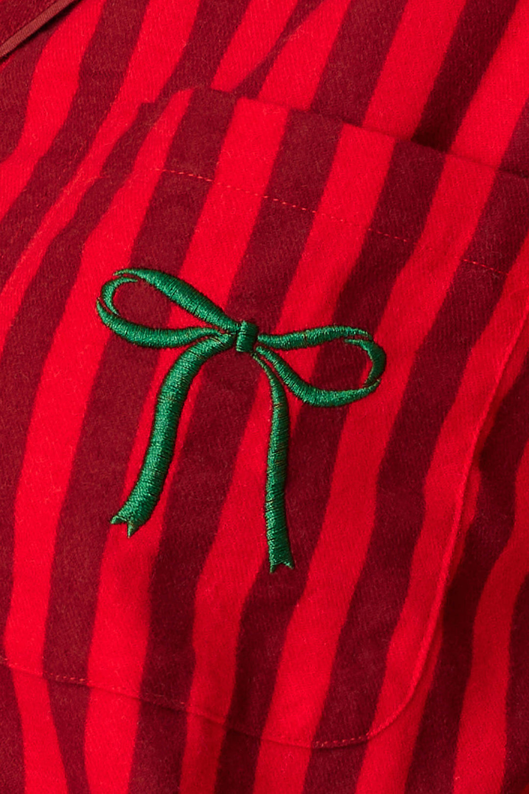 A close-up of the Icon 3-Piece Long Sleeve Flannel PJ Set by P.J. Salvage showcasing red fabric with vertical dark red stripes and a small green embroidered bow on the chest pocket.