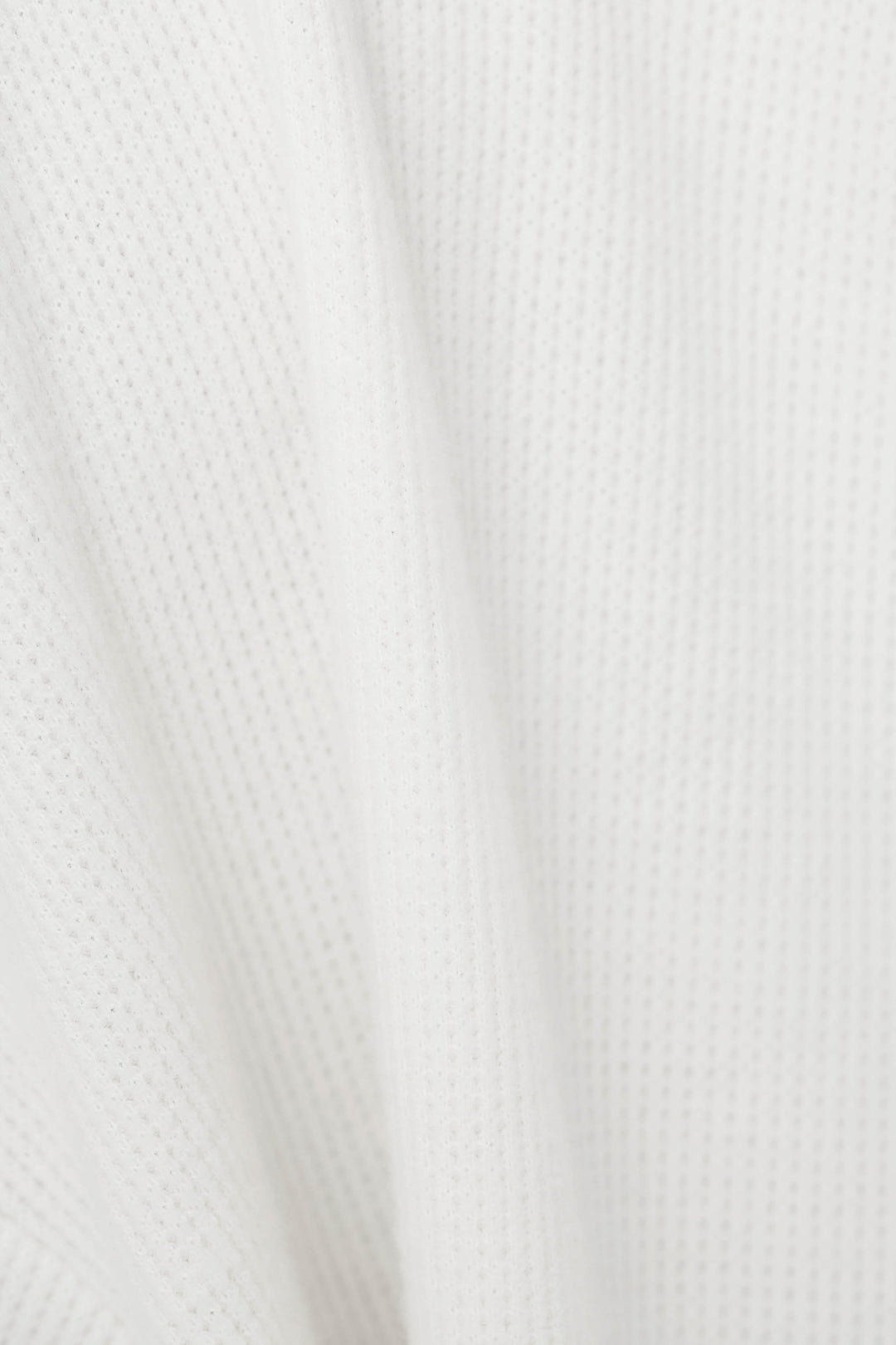 Close-up of a white textured fabric with a fine waffle pattern and soft folds.