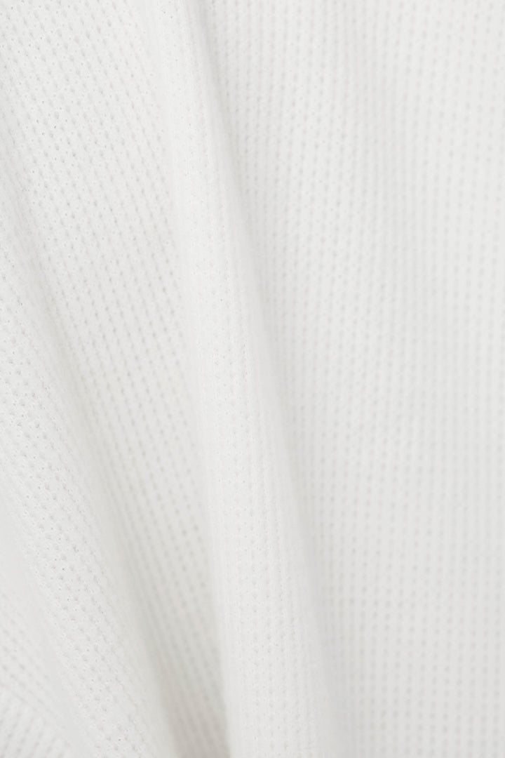 Close-up of a white textured fabric with a fine waffle pattern and soft folds.