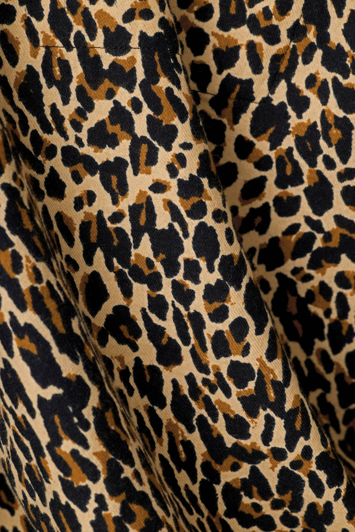 Close-up of leopard print fabric with black and dark brown spots on a warm beige background, showing soft folds in the material.