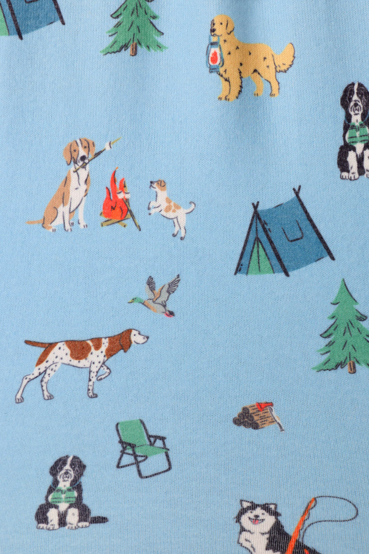 A close-up of a blue fabric featuring a repeating pattern of hand-drawn dogs camping illustrations including a dog making smores, trees, tents, ducks, camp chairs, dog with fishing poles and lanterns.