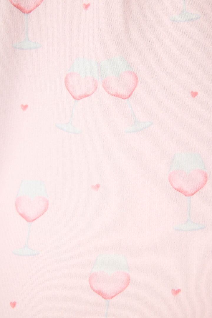 The P.J. Salvage Happy Hour Wine Glass Print 3-Piece Plus Size PJ Set features a light pink background with heart-shaped clusters of wine glasses filled with pink liquid, some clinking together, and scattered small pink hearts.