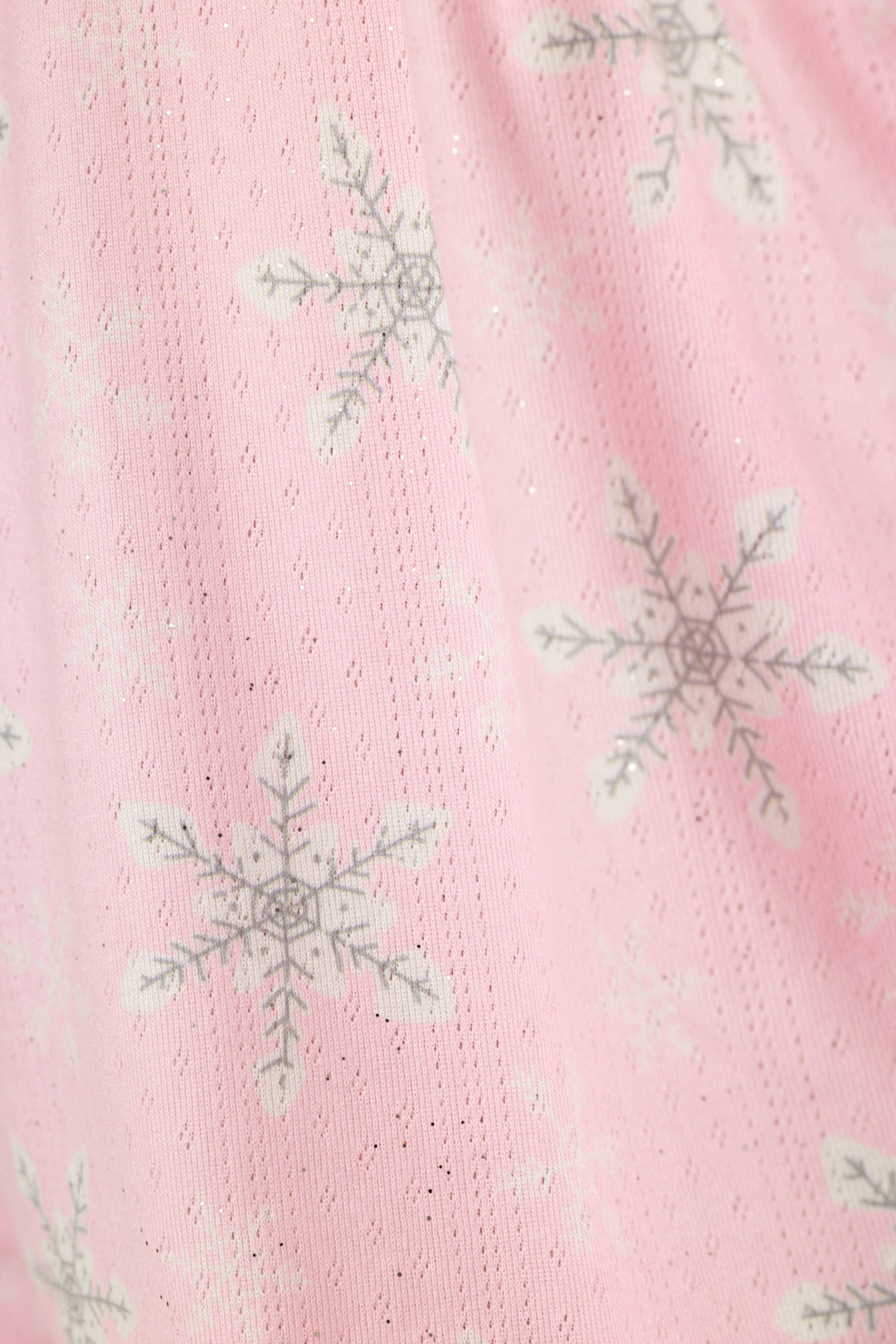 A close-up of a pink textured fabric with a repeating pattern of white and gray snowflakes with subtle sparkle.