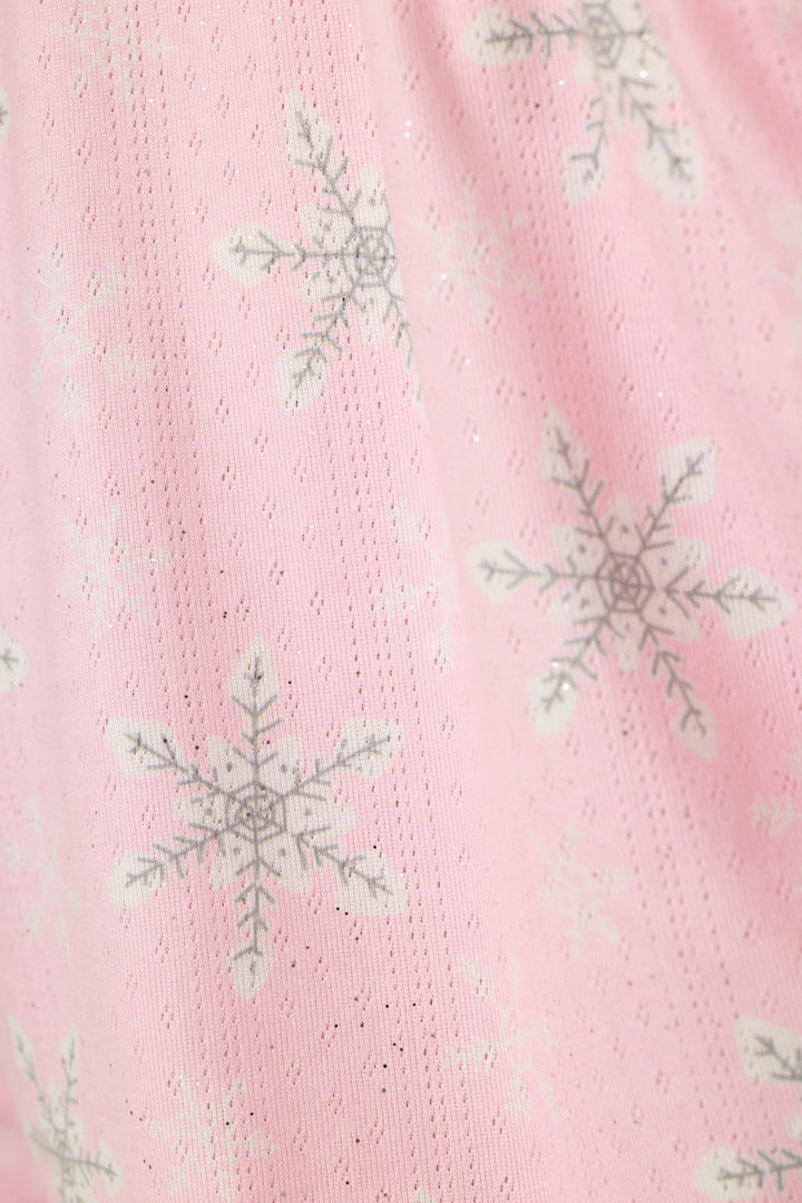 A close-up of a pink textured fabric with a repeating pattern of white and gray snowflakes with subtle sparkle.