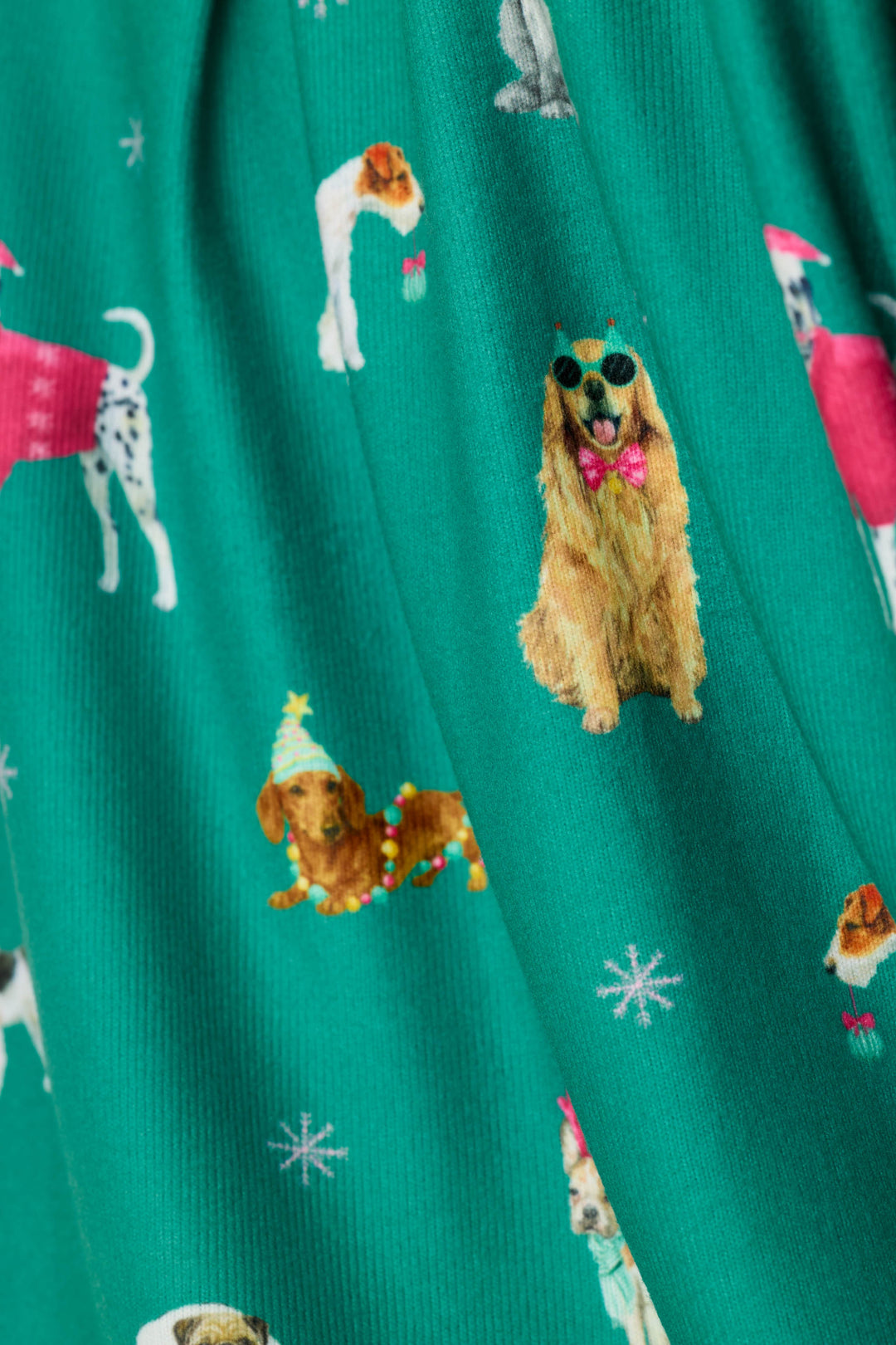 A close-up of a green fabric with an all-over print of various dog illustrations in different poses, some wearing festive and colorful accessories, with small white snowflake motifs.