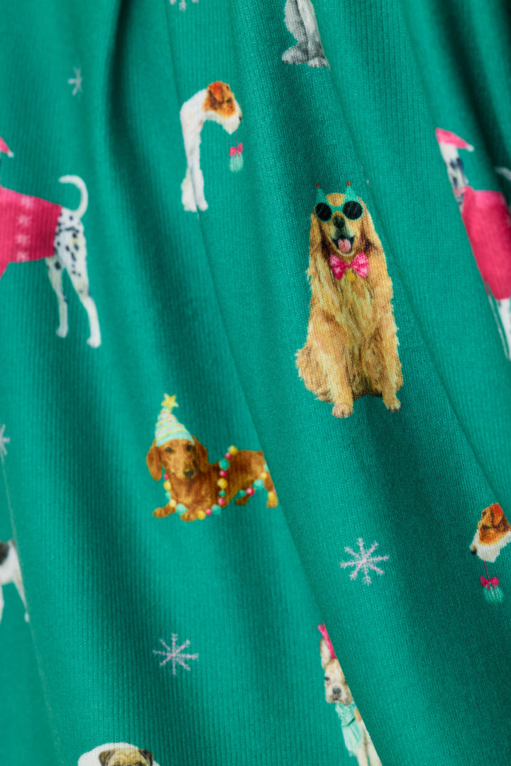 A close-up of a green fabric with an all-over print of various dog illustrations in different poses, some wearing festive and colorful accessories, with small white snowflake motifs.