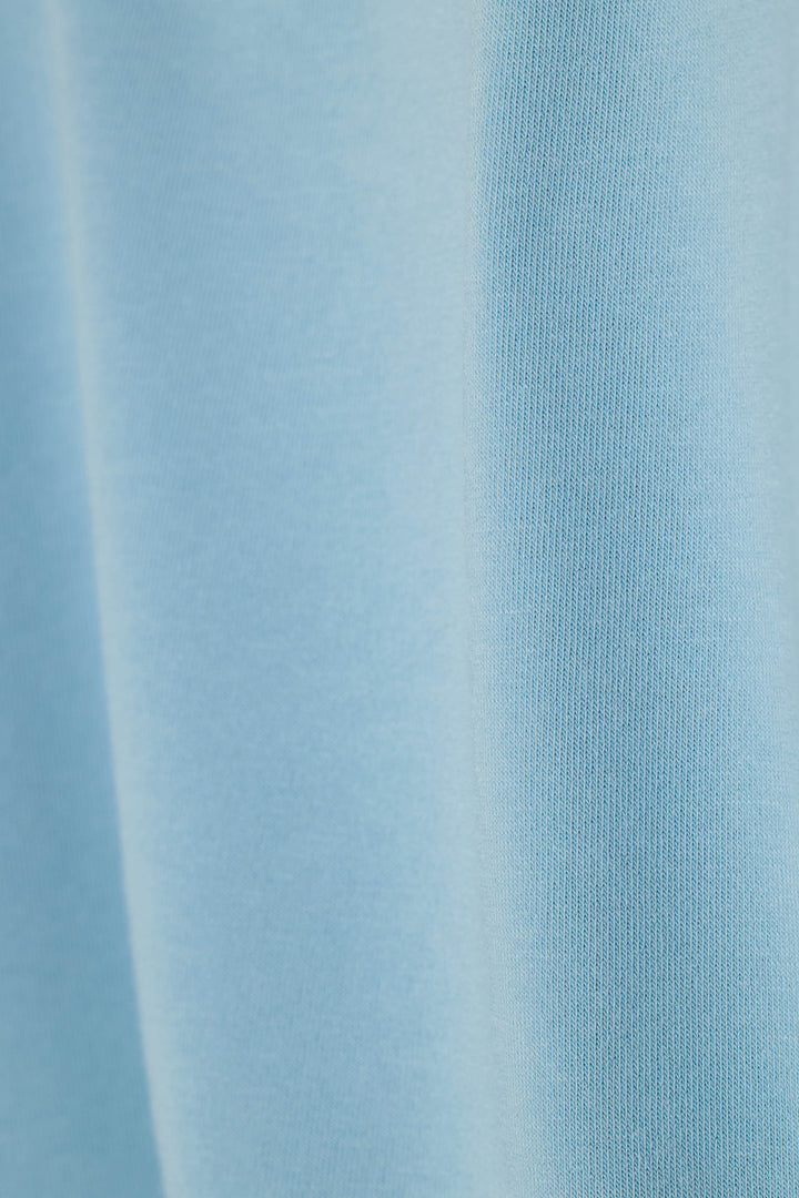 A close-up of light blue ribbed knit fabric with soft vertical folds and a smooth texture.