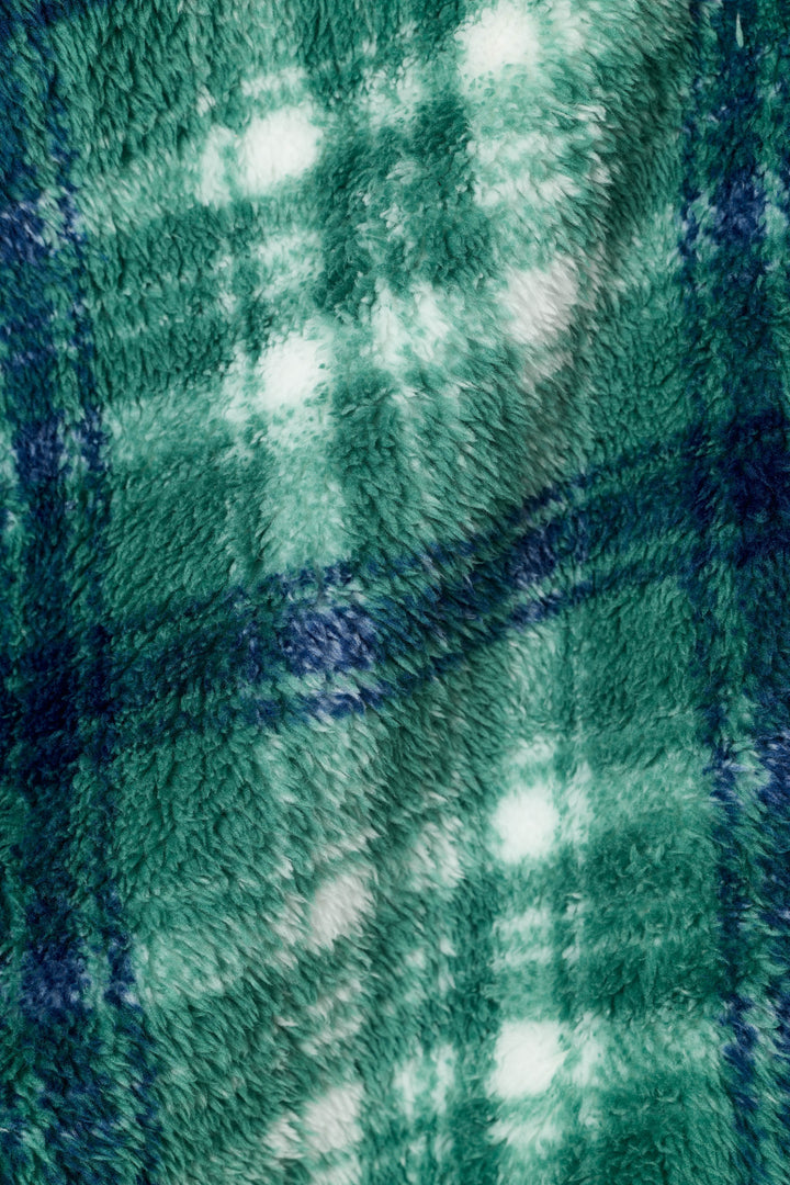 A close-up of a plush, fuzzy fabric with a green and navy plaid pattern and white accents.