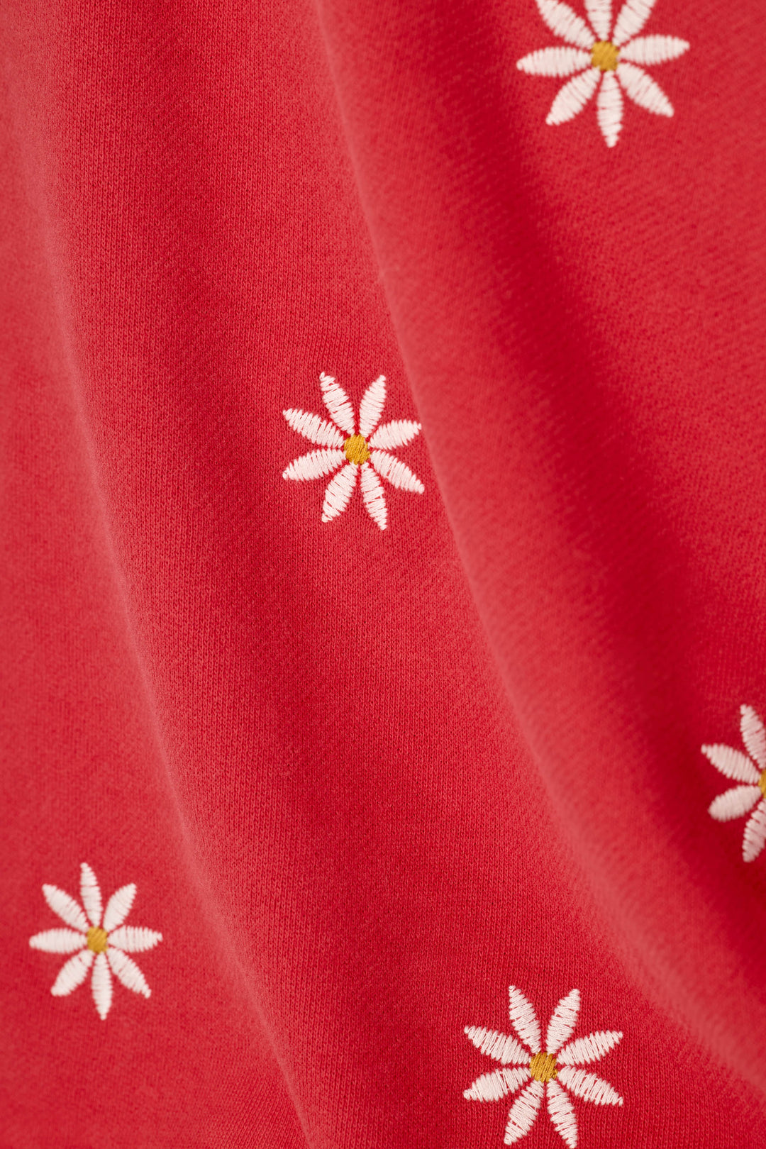 A close-up of a red fabric with a repeating pattern of white daisy flowers with yellow centers.