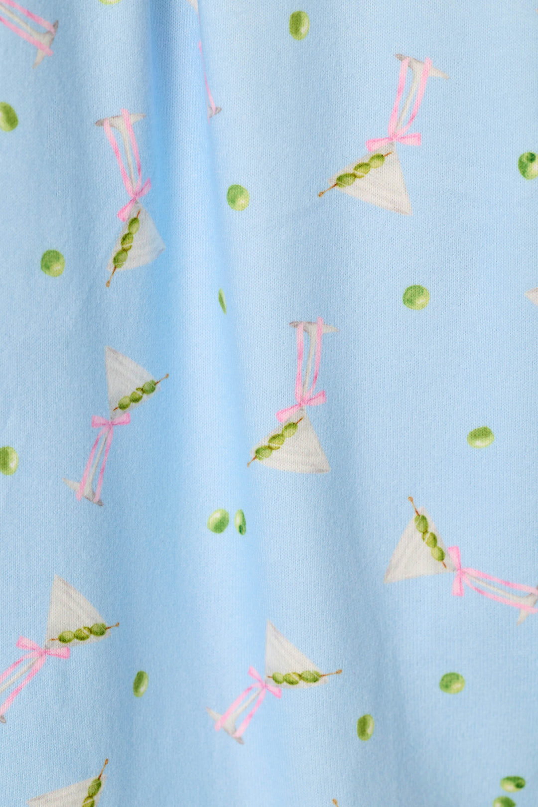The Olive You Martini Print by P.J. Salvage is a light blue fabric adorned with a playful pattern of green peas in pods and small white triangles, each tied with pink bows, scattered throughout.