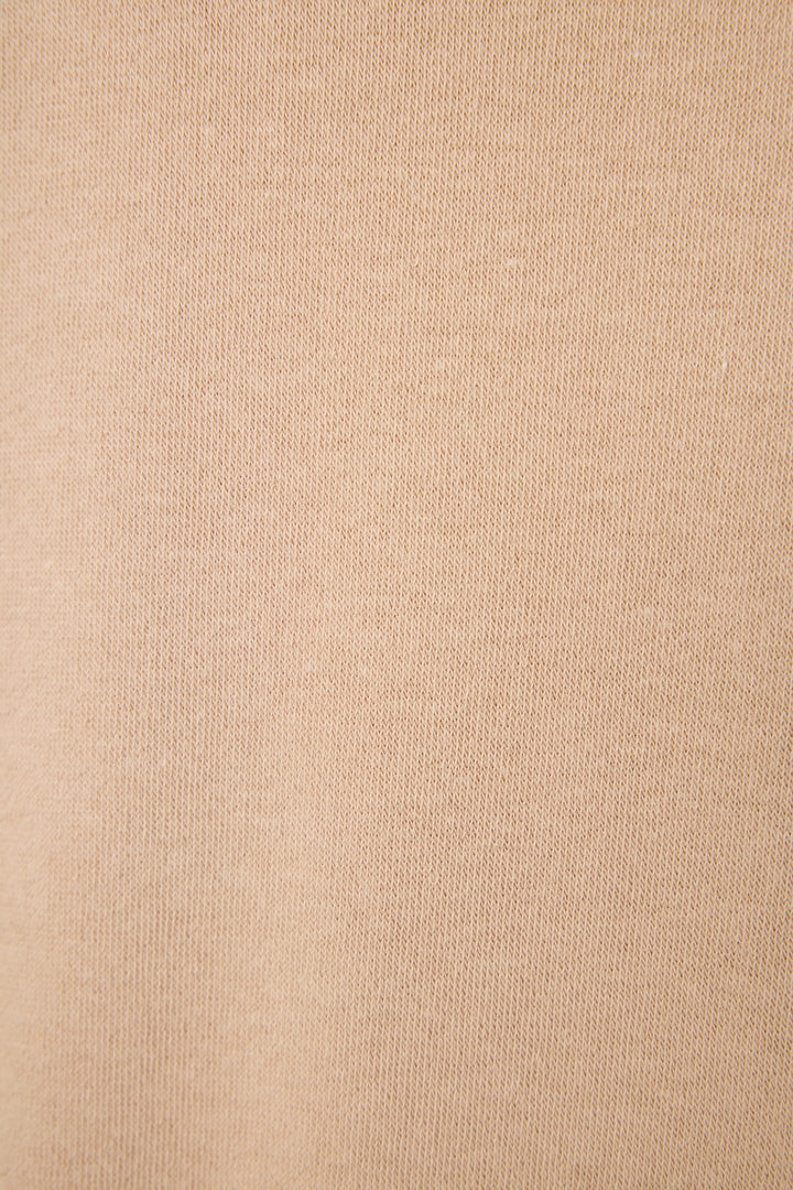 Close-up of the Palms Away Warm Taupe fabric featuring soft beige fabric with a fine, slightly ribbed knit texture and subtle diagonal lines for a cozy lounge look.