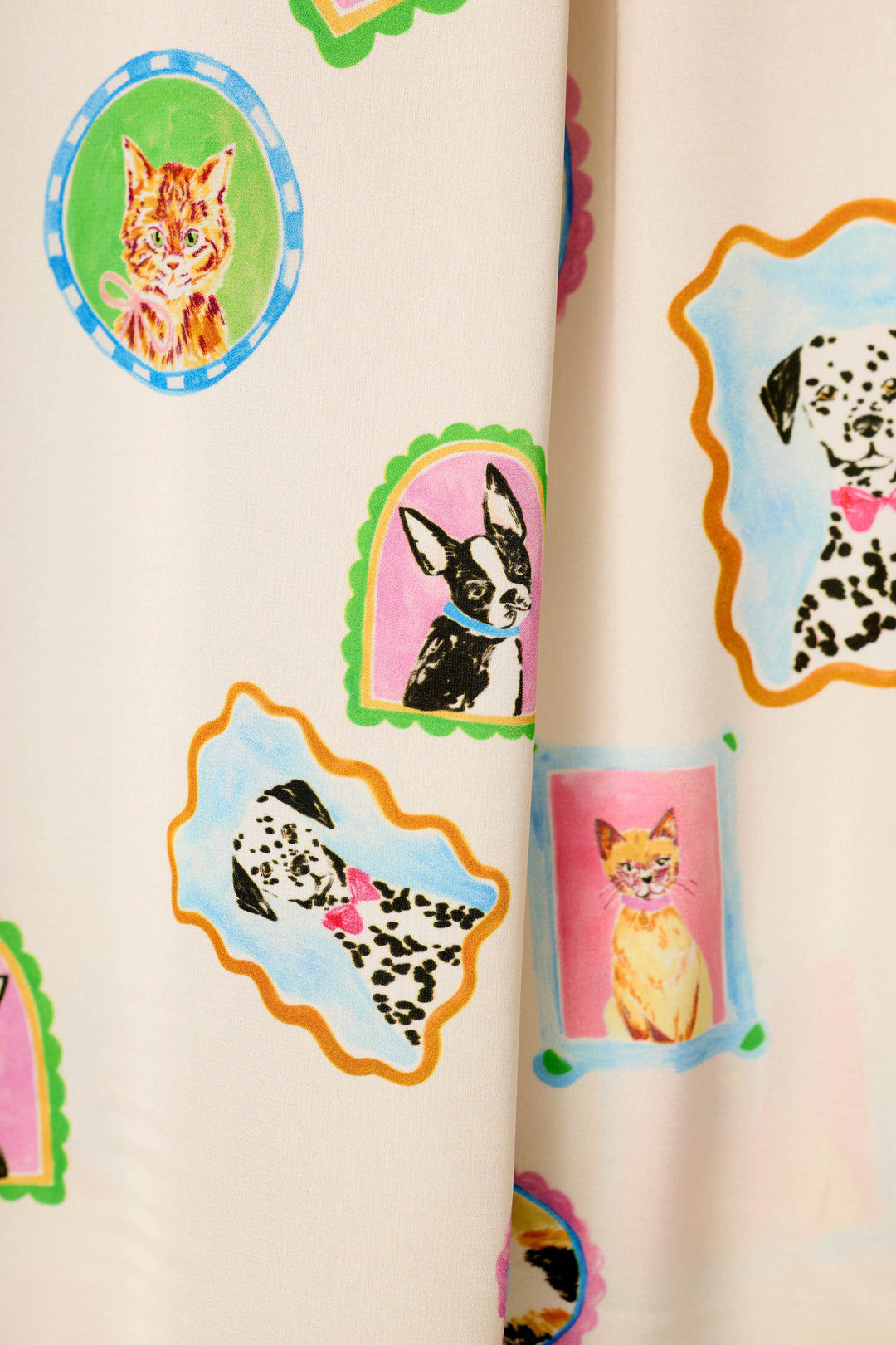 The Picture Purrfect Pet Portrait Print in a Sateen by P.J. Salvage is a cream-colored fabric adorned with playful, pastel portrait-style illustrations of cats and dogs—including Dalmatian and Boston Terrier breeds—set within colorful, framed designs.