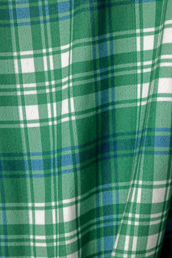 A close-up of a green plaid fabric with white and blue stripes, showing a soft woven texture.