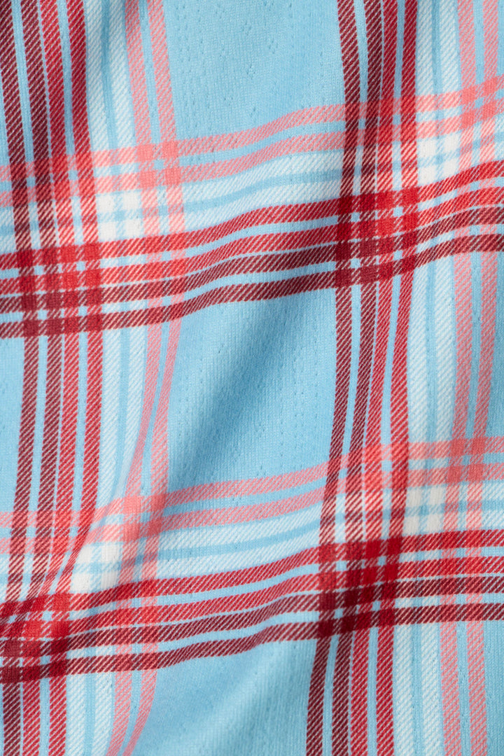A close-up of a plaid fabric pattern featuring a light blue background with red and white intersecting stripes.
