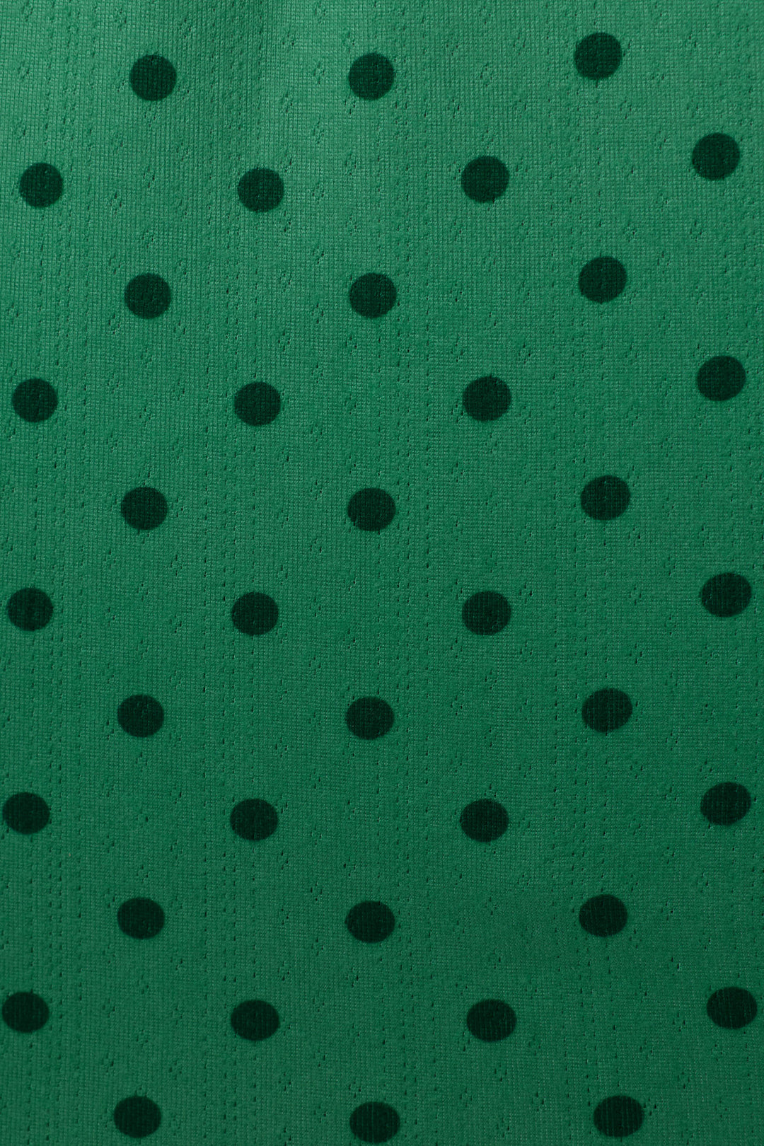 A close-up of a green textured fabric with a repeating pattern of black polka dots.