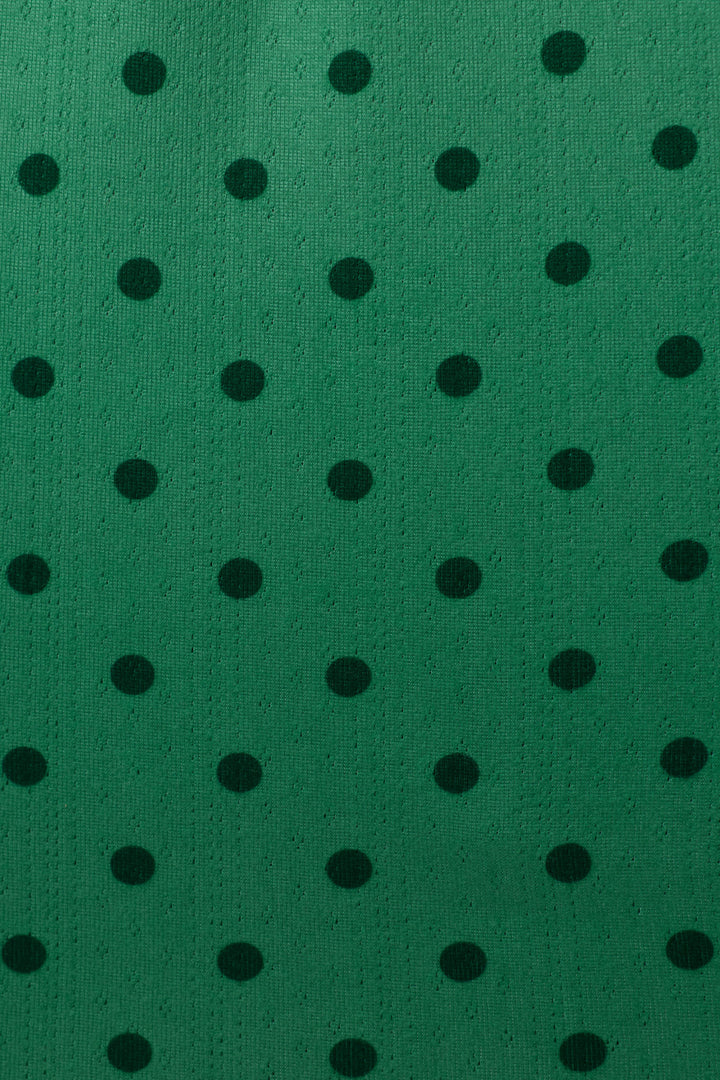 A close-up of a green textured fabric with a repeating pattern of black polka dots.