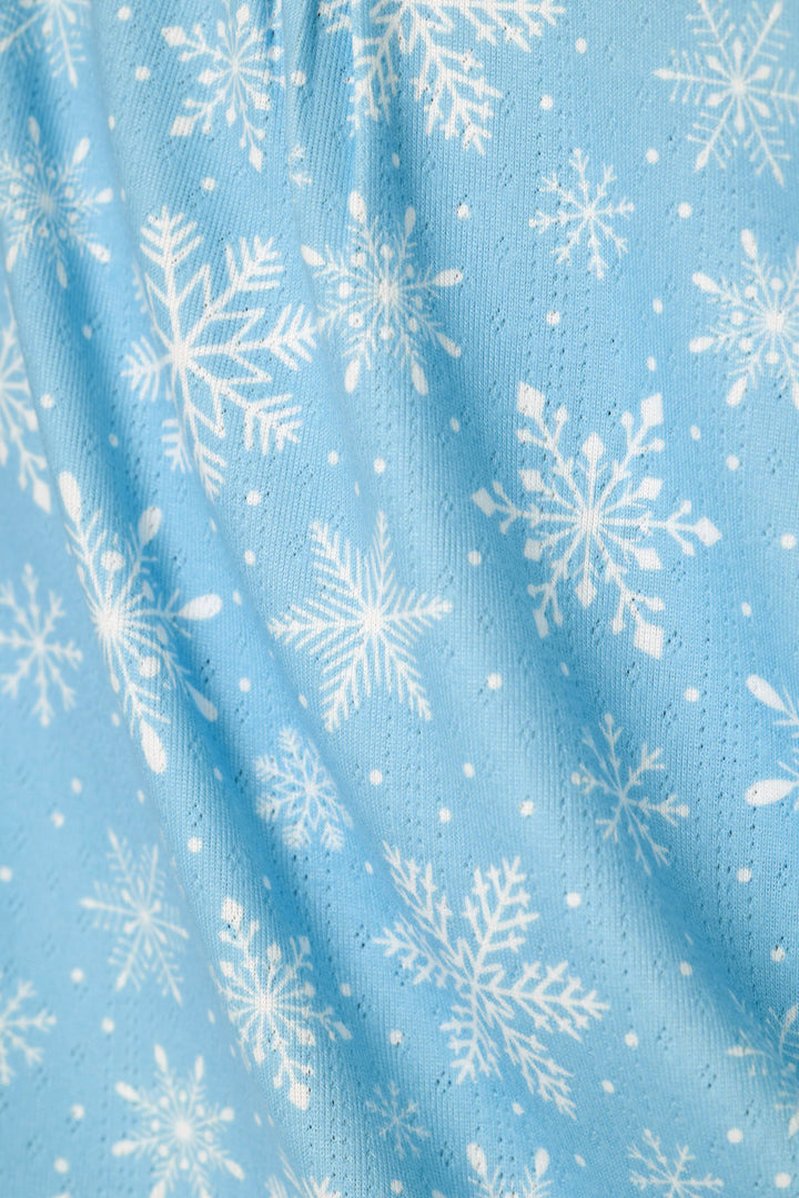 A close-up of light blue fabric with a white snowflake and snow dot pattern, showing a fine pointelle knit texture and soft folds.