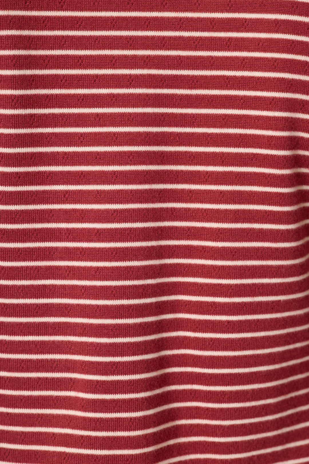 A close-up of a red knit fabric with thin, evenly spaced horizontal white stripes.