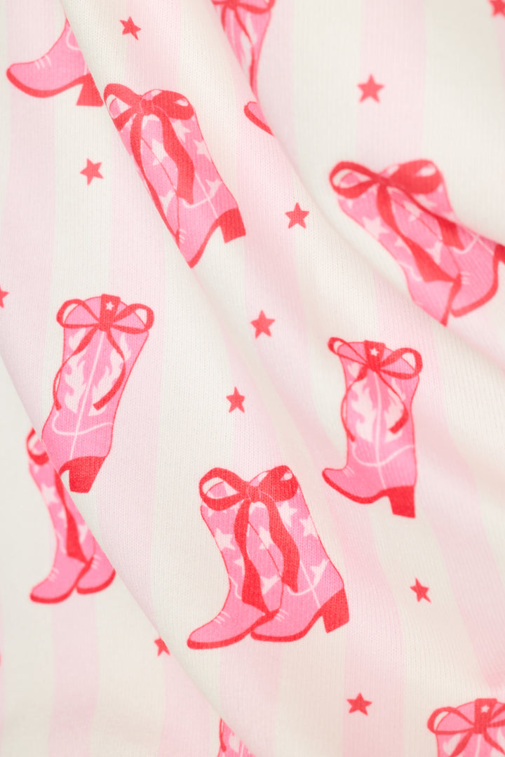 A close-up of a light pink fabric with a repeating pattern of pink cowboy boots and small red stars and faint pink stripes.
