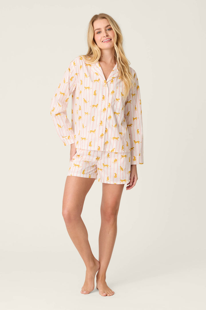 A person stands barefoot against a plain background wearing the Afterparty Poplin Cheetah Charm Short PJ Set by P.J. Salvage—a button-up long-sleeve shirt and shorts featuring a cheetah print on soft poplin fabric.