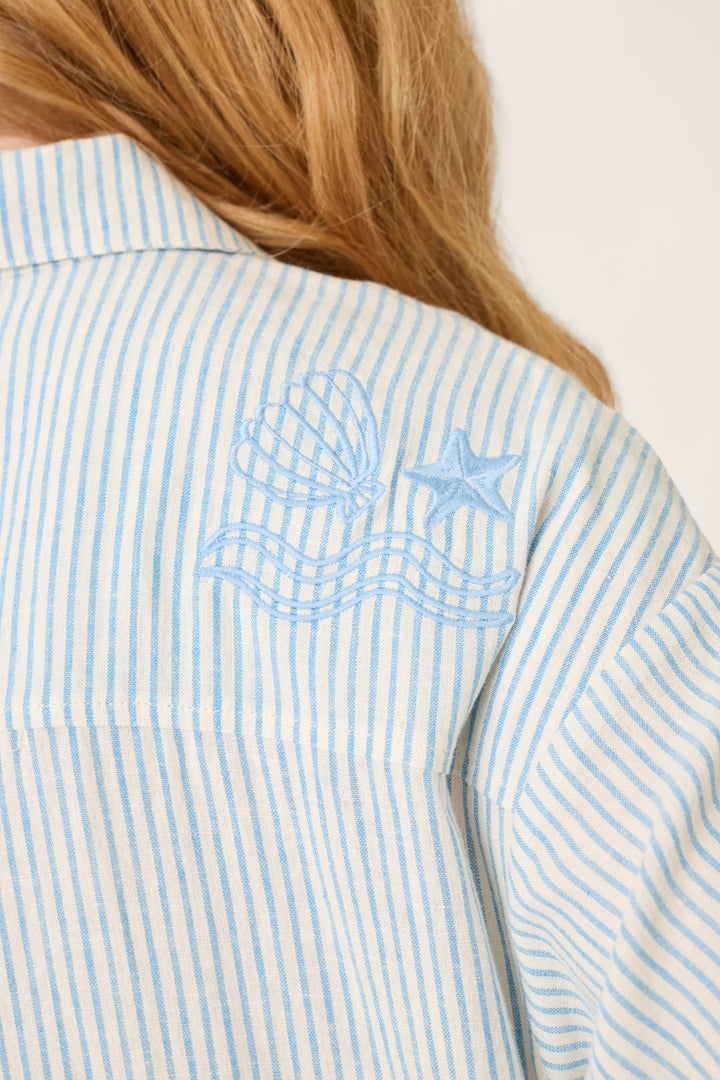 Light blue and white vertical striped fabric with embroidered shell, star, and wavy lines on the shoulder.