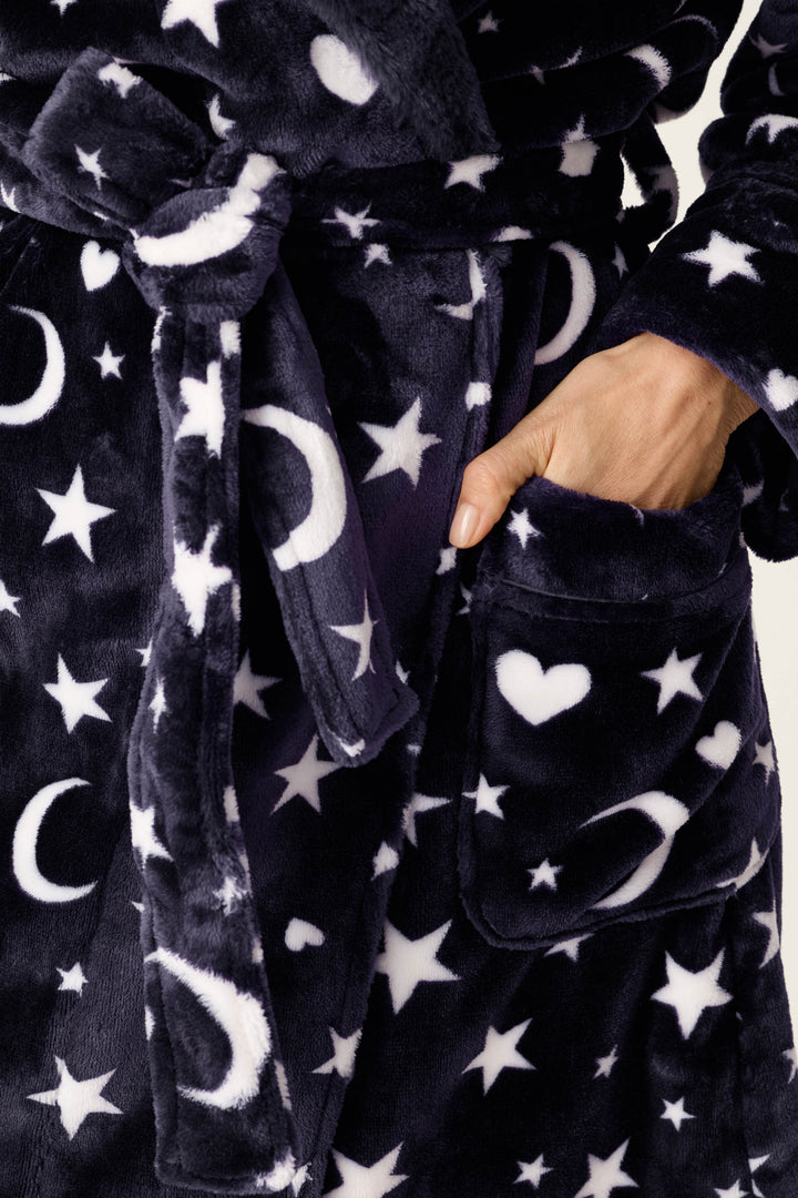 Close-up of a plush robe in dark navy with a white celestial print of stars, moons, and hearts, featuring a side pocket and a hand reaching into the pocket.