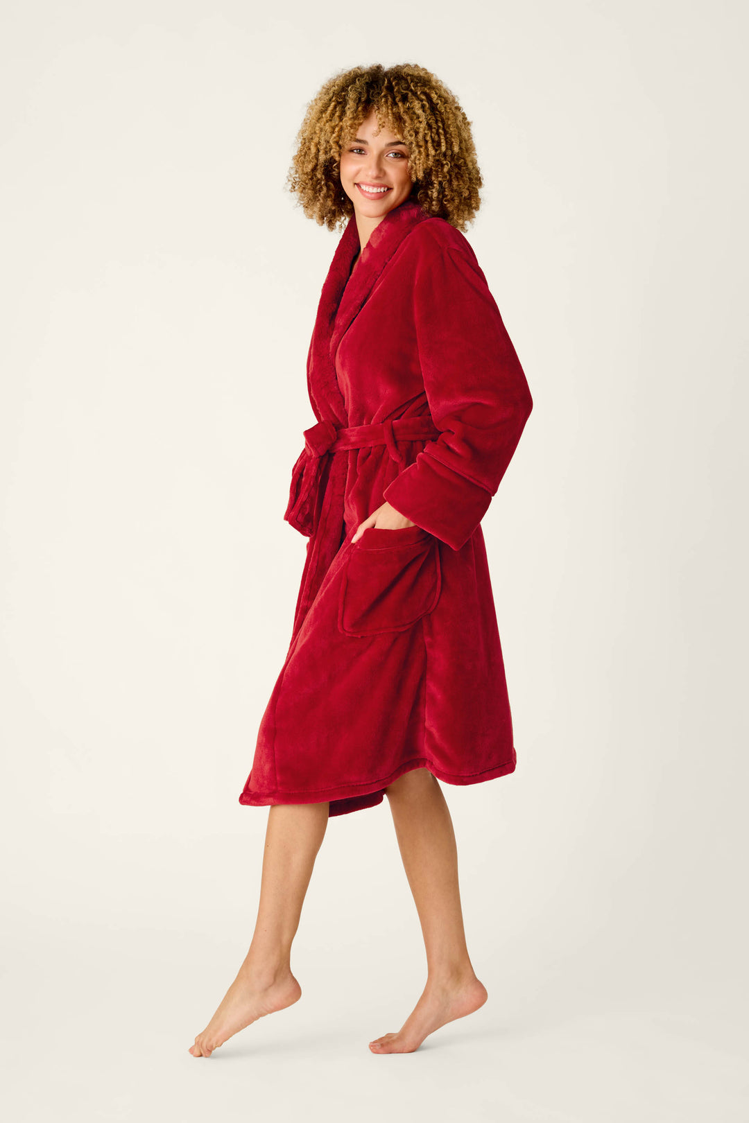 A person with curly hair smiles while wearing a cozy red Luxe Plush Red Robe by P.J. Salvage, featuring a tie waist and side pockets.