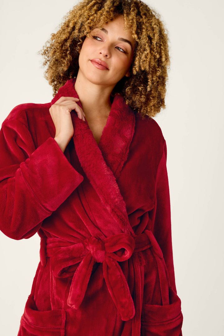 A person with curly hair wears a cozy, plush red Luxe Plush Red Robe by P.J. Salvage featuring a shawl collar and tie waist.
