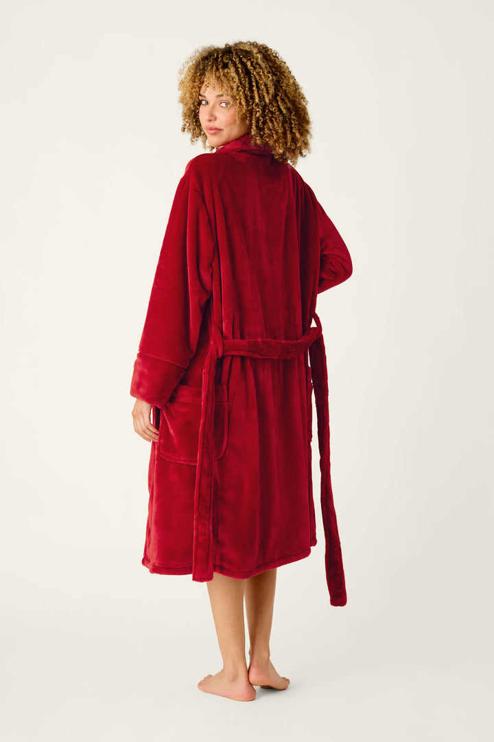 A woman with curly hair wearing a cozy, knee-length red Luxe Plush Red Robe by P.J. Salvage with a matching tie belt.