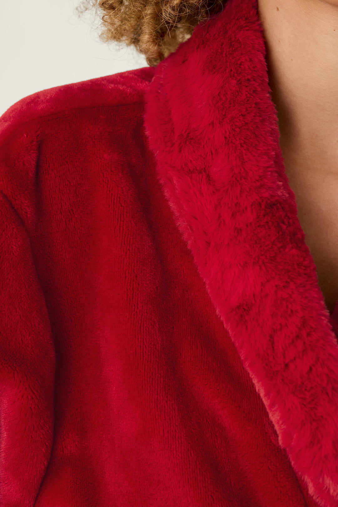 Close-up of a person wearing a cozy, bright red Luxe Plush Red Robe by P.J. Salvage, featuring a thick, plush faux-fur collar.