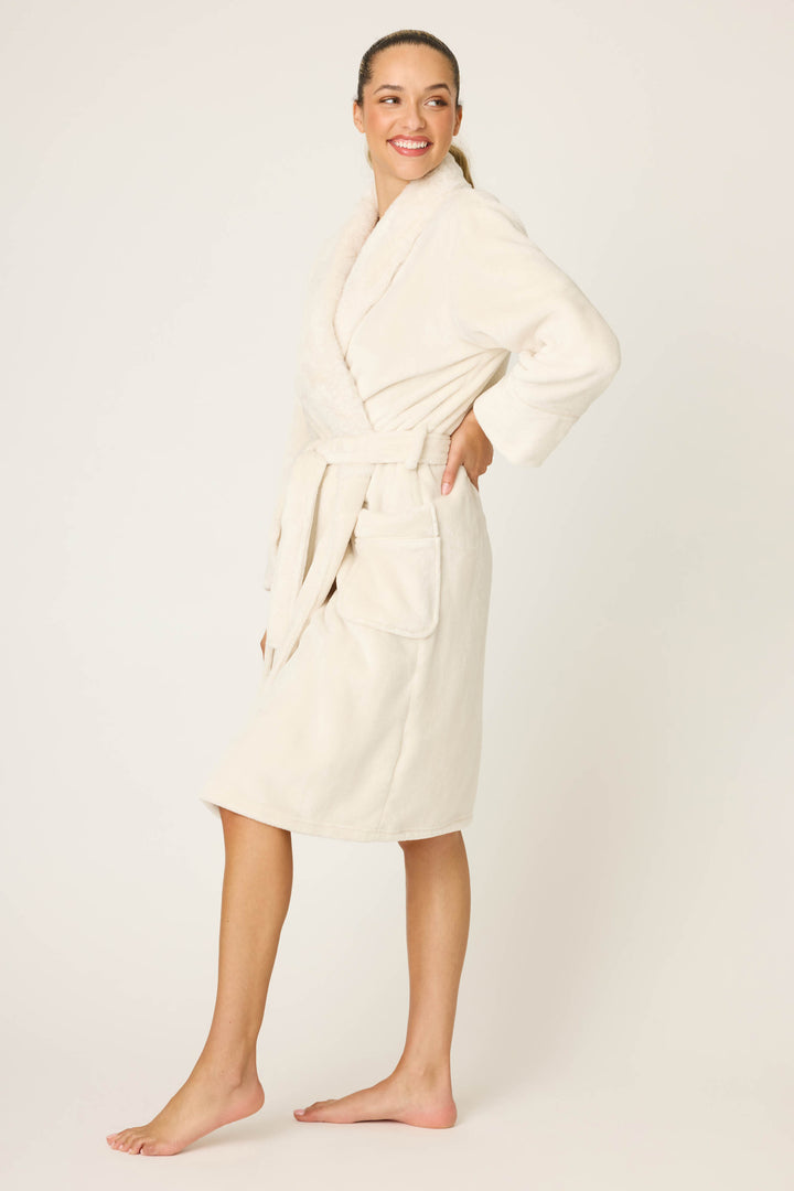 A person stands barefoot against a plain background, smiling and wearing the P.J. Salvage Luxe Plush Solid Ivory Robe, featuring a belt and patch pockets.