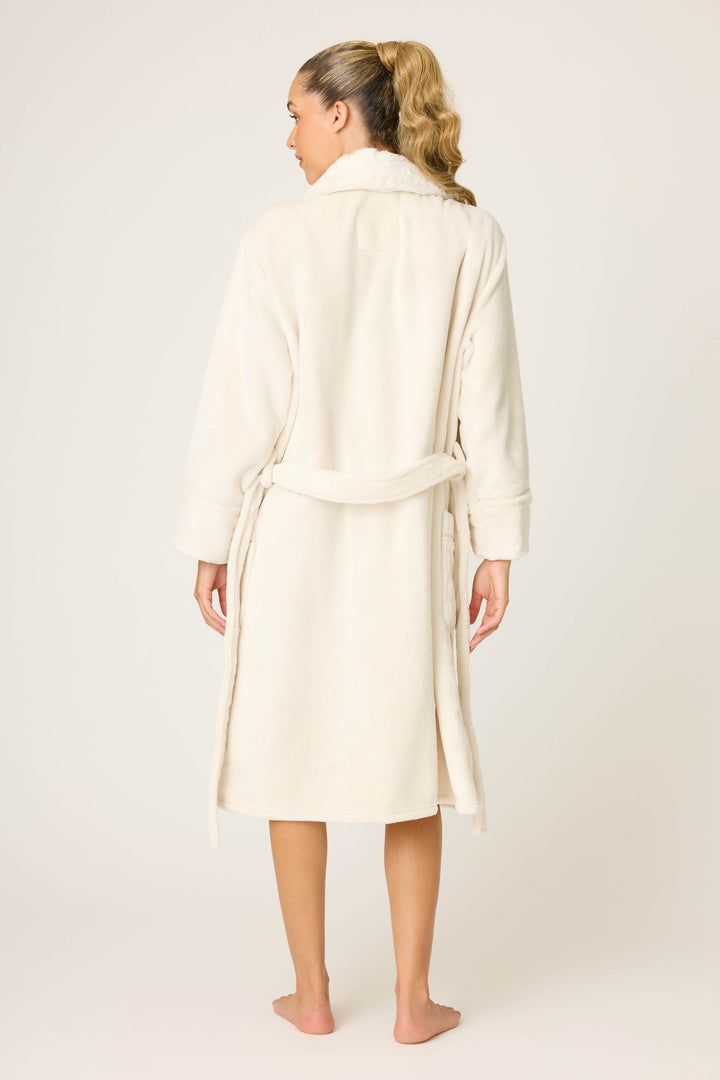 A person with long, blond hair in a ponytail is standing barefoot, facing away from the camera, wearing the P.J. Salvage Luxe Plush Solid Ivory Robe, which is knee-length with a belt tied at the waist.