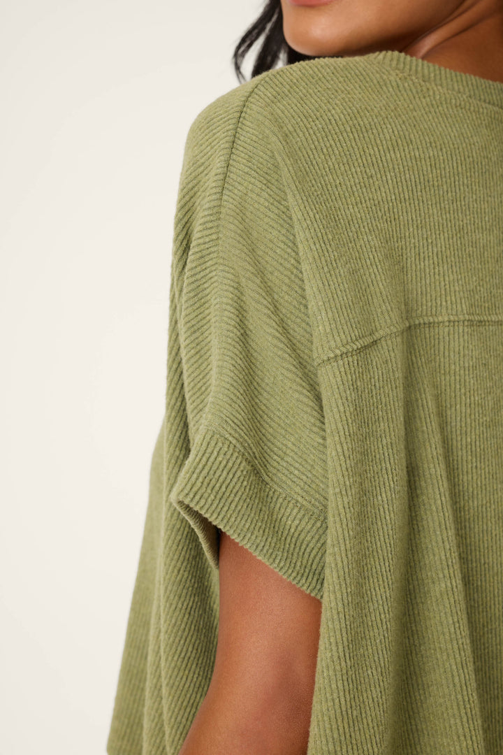 Close-up of a person in the P.J. Salvage Olive You Forever Lounge Set, featuring a loose, short-sleeved, ribbed olive green top. Only part of their face, shoulder, and upper arm is shown against a plain light background.