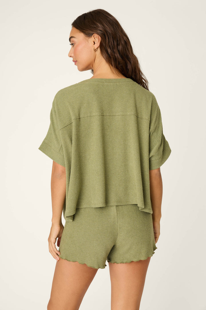 A woman with long brown hair is seen from the back wearing the P.J. Salvage Olive You Forever Lounge Short Sleeve Top and matching shorts, both featuring scalloped hems, against a plain light background.