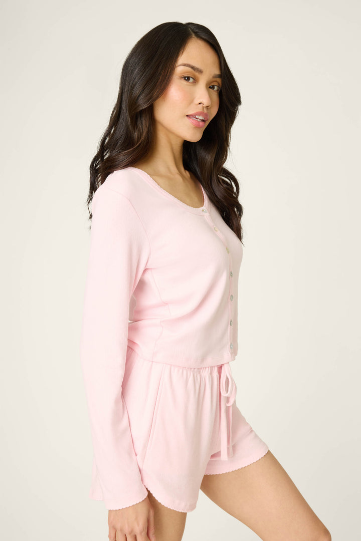 A woman with long dark hair models the P.J. Salvage Pointelle Essentials Ballet Pink Cardigan, standing sideways and looking toward the camera against a plain light background.