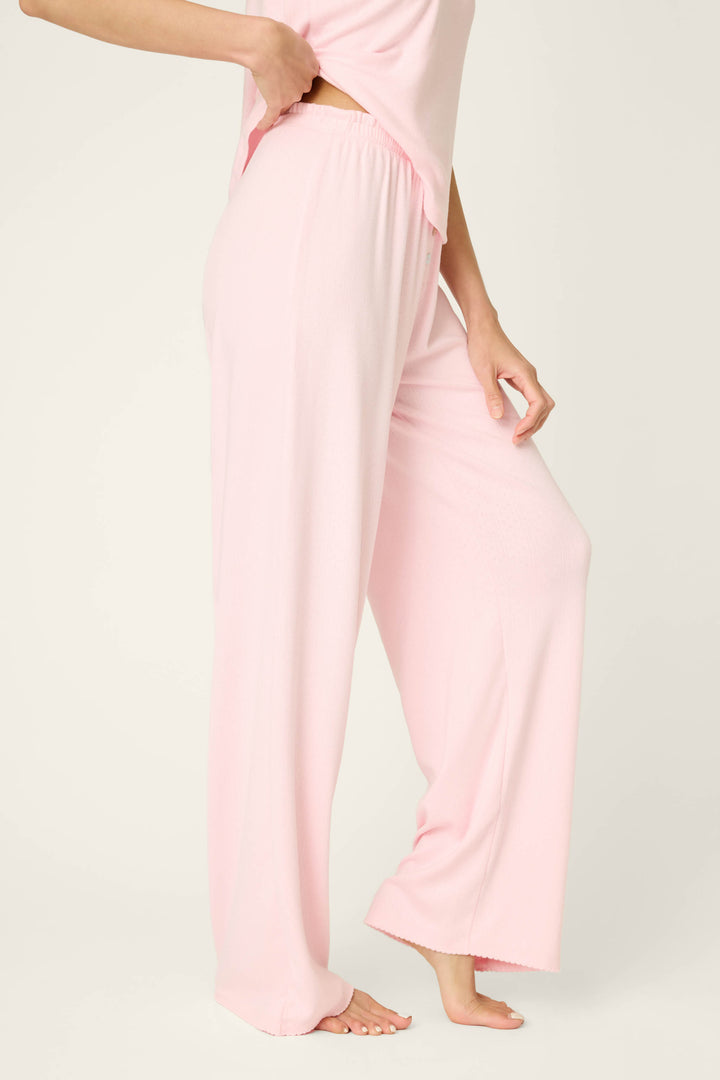 A person models P.J. Salvage Pointelle Essentials Ballet Pink Open Leg Pants, seen from the waist down with one leg lifted and a hand at the waistband. The background is plain and light-colored.