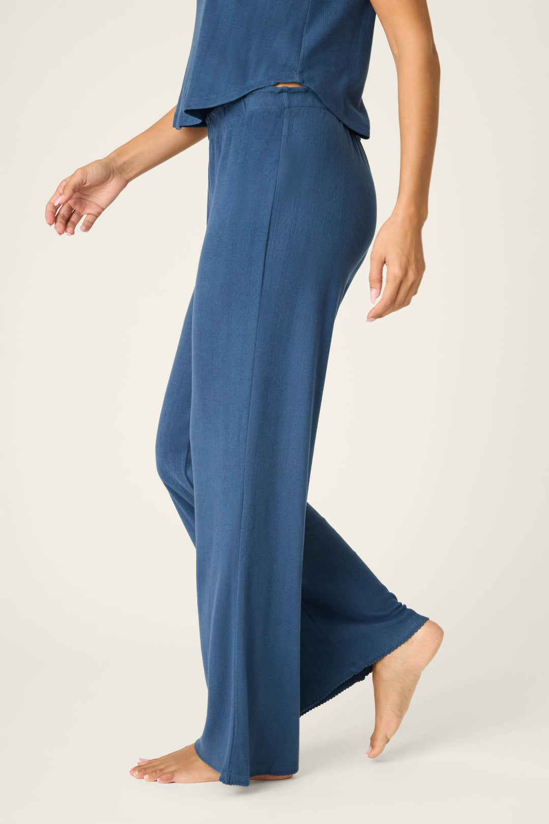 A person stands barefoot in P.J. Salvage Pointelle Essentials Deep Sea Open Leg Pants with an adjustable drawstring, paired with a matching blue top. The photo is cropped from shoulders down against a neutral background.