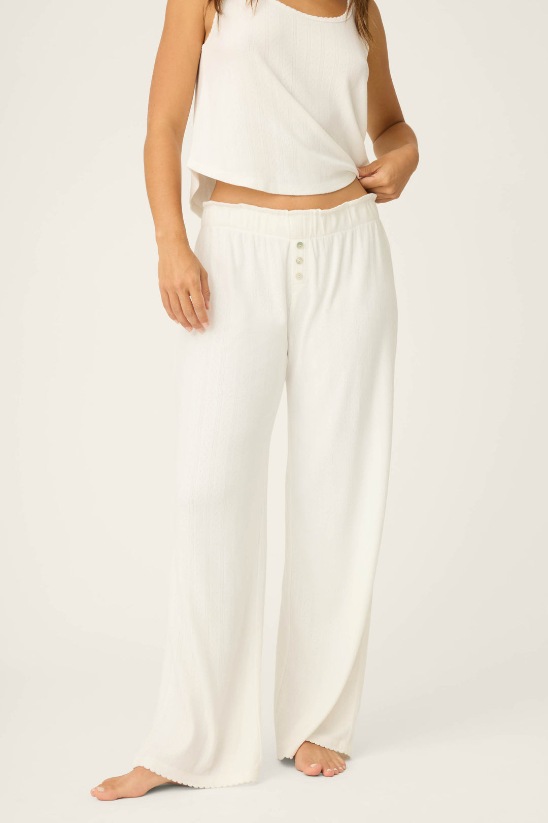 A person stands barefoot wearing P.J. Salvage Pointelle Essentials Ivory Open Leg Pants with a buttoned waist, paired with a matching sleeveless white top, shown from shoulders down against a plain background.