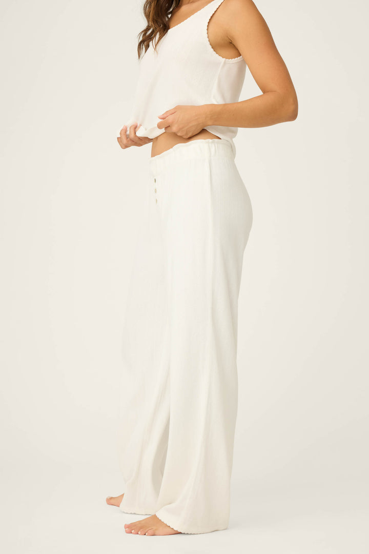A person stands barefoot, wearing P.J. Salvage Pointelle Essentials Ivory Open Leg Pants and a loose white sleeveless top. The light, comfortable outfit shows only the lower face and body; the background is plain, off-white.