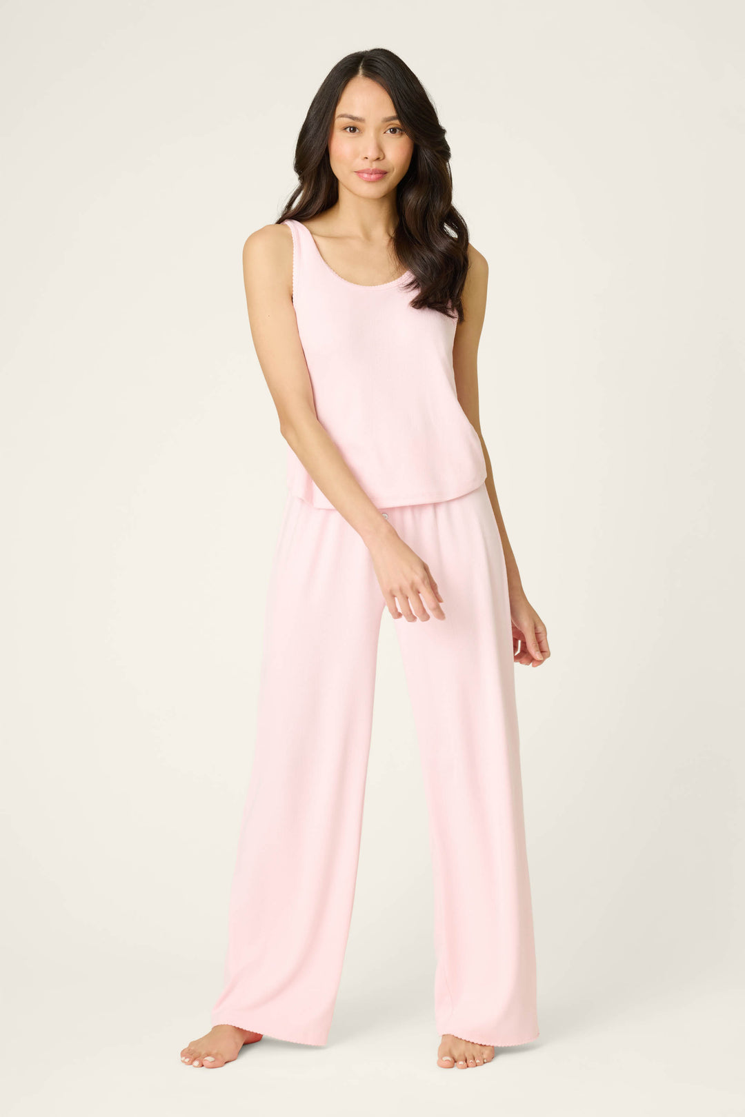A woman with long, dark hair models the P.J. Salvage Pointelle Essentials Ballet Pink PJ Set— a sleeveless, loose-fitting pajama set—barefoot against a plain, light background.