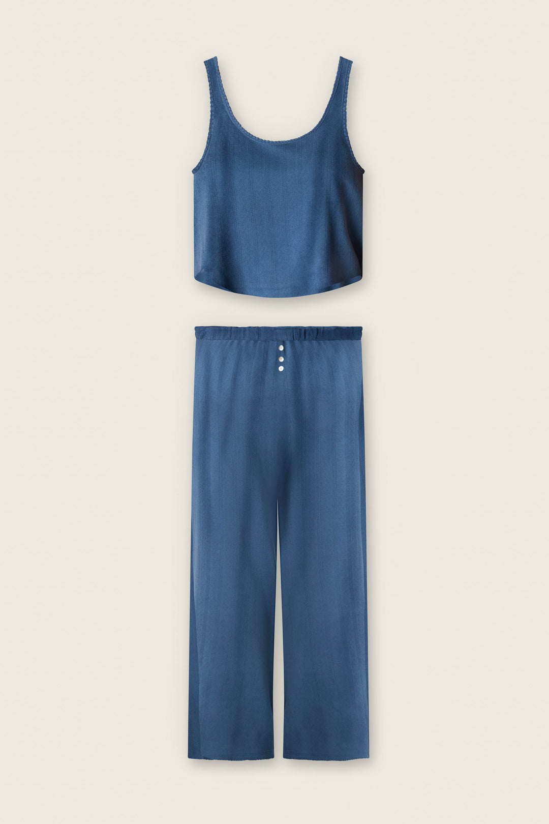 The P.J. Salvage Pointelle Essentials Deep Sea PJ Set is a chic two-piece with a blue silky sleeveless crop top and wide-leg pants with an elastic waistband and three white buttons—perfect for stylish lounging.