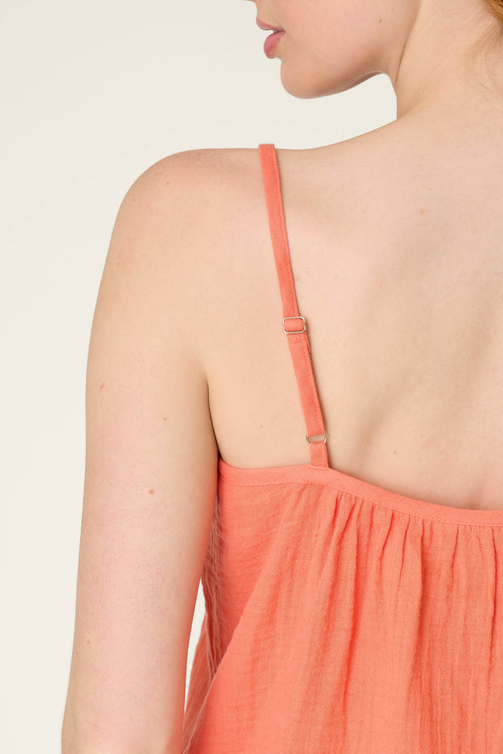 A close-up of a person's back and shoulder wearing a sleeveless top with thin adjustable straps, against a plain light background.