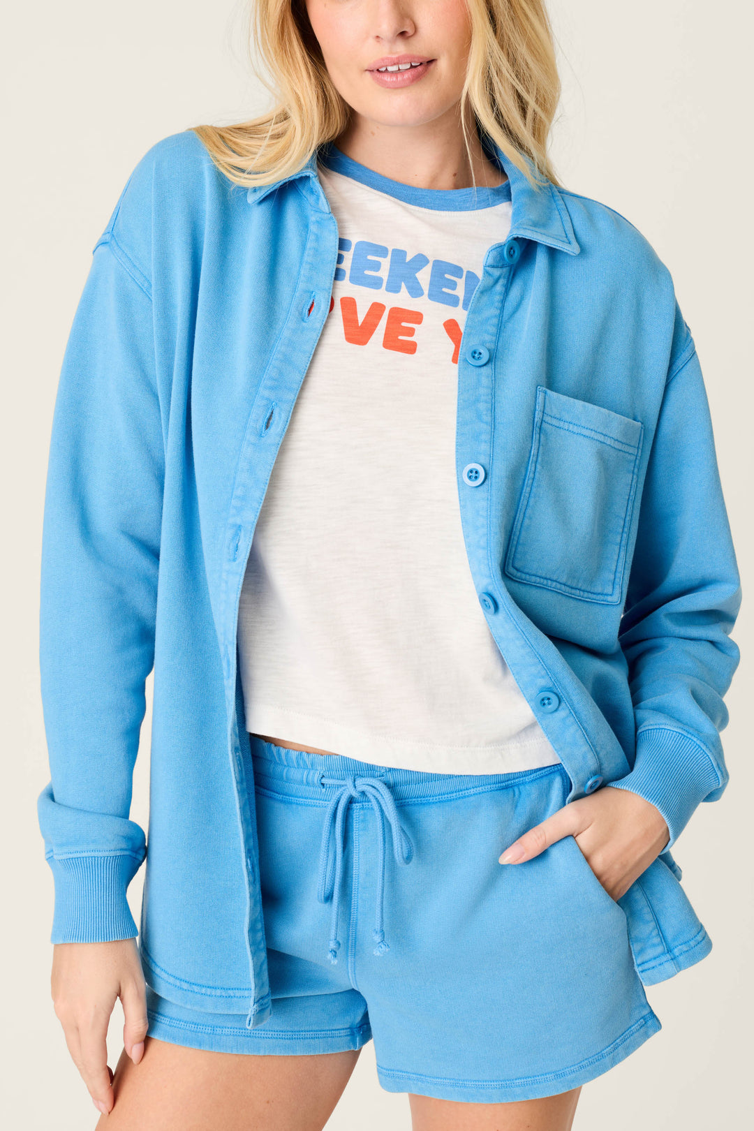 A person wears the P.J. Salvage Washed Away Marine Blue Shirt Jacket with a button-front over matching drawstring shorts and a white tee with colorful text, showcasing the relaxed silhouette from shoulders to mid-thighs against a neutral background.