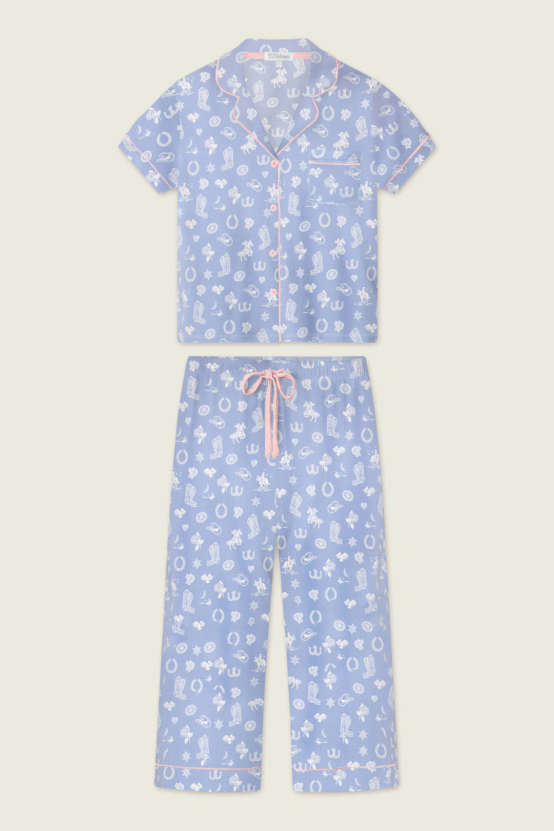 The Whimsy Lone Star Love Cropped PJ Set by P.J. Salvage features a light blue, two-piece set with a short-sleeve button-up top and cropped drawstring pants, decorated with a white cartoon print, pink piping, and a pink waistband tie.