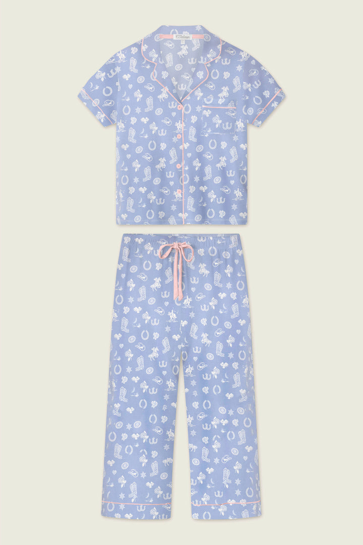 The Whimsy Lone Star Love Cropped PJ Set by P.J. Salvage features a light blue, two-piece set with a short-sleeve button-up top and cropped drawstring pants, decorated with a white cartoon print, pink piping, and a pink waistband tie.