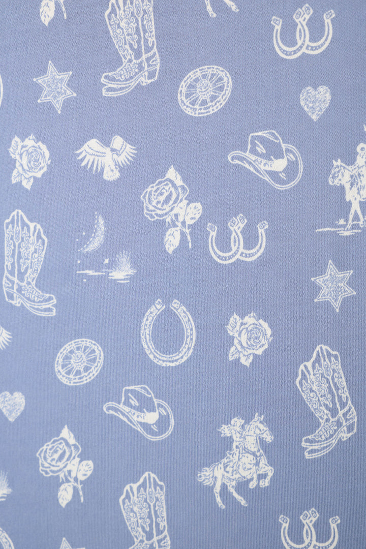 The Whimsy Lone Star Love Cropped PJ Set by P.J. Salvage features light purple fabric adorned with white Western-inspired prints, including cowboy boots, horseshoes, hats, roses, stars, a bird, horse and rider, lasso, heart, and campfire.
