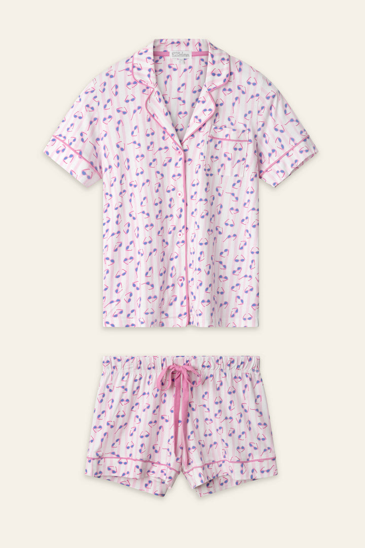 The Whimsy Retro Shades Short PJ Set by P.J. Salvage includes a short-sleeve button-up top and drawstring shorts with a pink and purple flamingo print on white, finished with pink trim.
